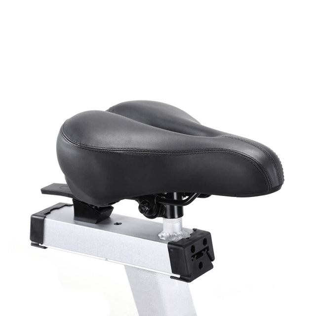 The Blitz Air Bike by Bells of Steel features a close-up of its black contoured padded seat mounted on a silver frame. The seat, designed for comfort and stability in home gyms, is showcased against a plain white background, emphasizing its sleek design.