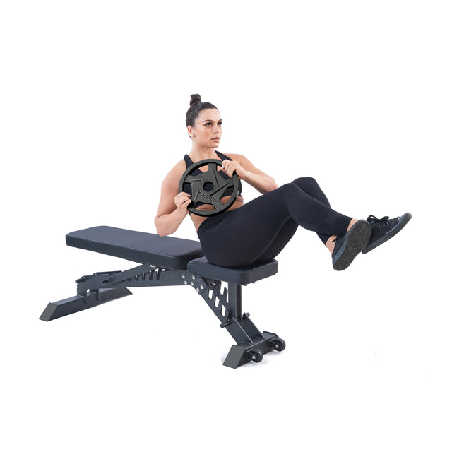 A person in workout attire sits on a fitness bench with precision grip handles, performing a Russian twist using a Black Mighty Grip Olympic Weight Plate by Bells of Steel. Focused and balancing with elevated legs, the individual exudes strength against the plain white background.