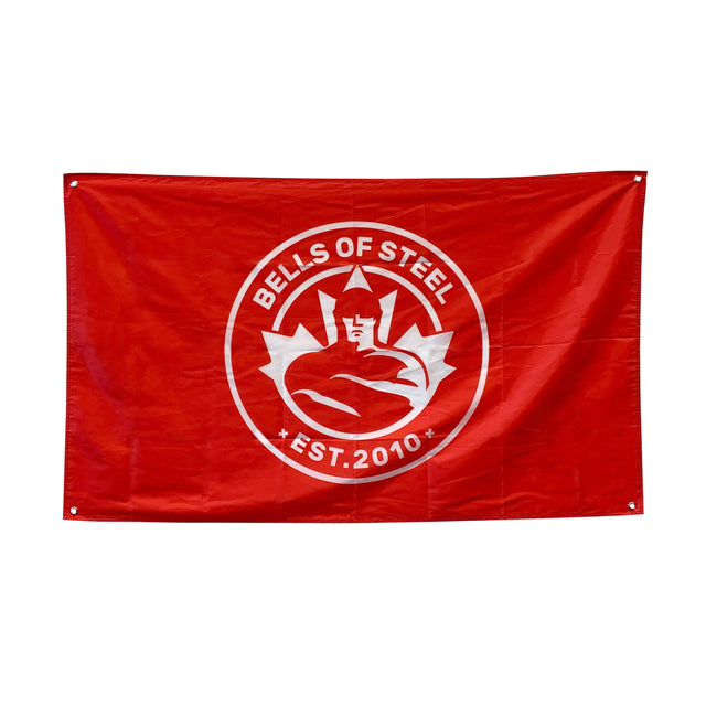 A red flag from Bells of Steel features a white logo of a muscular figure in a helmet within a circle, "BELLS OF STEEL" above, and "EST. 2010" below. Ideal home gym decor to energize your workout space.