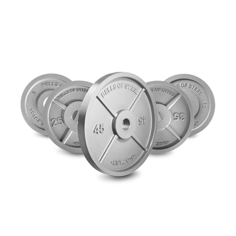 Five Bells of Steel Machined Iron Olympic Weight Plates of different sizes are arranged in a semi-circle, with a 45 lb plate upright in the center. Each plate features precision hole fit and is labeled with its weight and brand name.