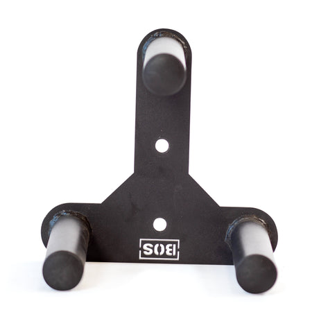 The Bells of Steel Change Plate Storage Pegs is a black metal wall mount bracket with three cylindrical pegs arranged in a triangle, ideal for organizing Olympic change plates. It features two mounting holes and an upside-down "SIS" logo at the bottom.