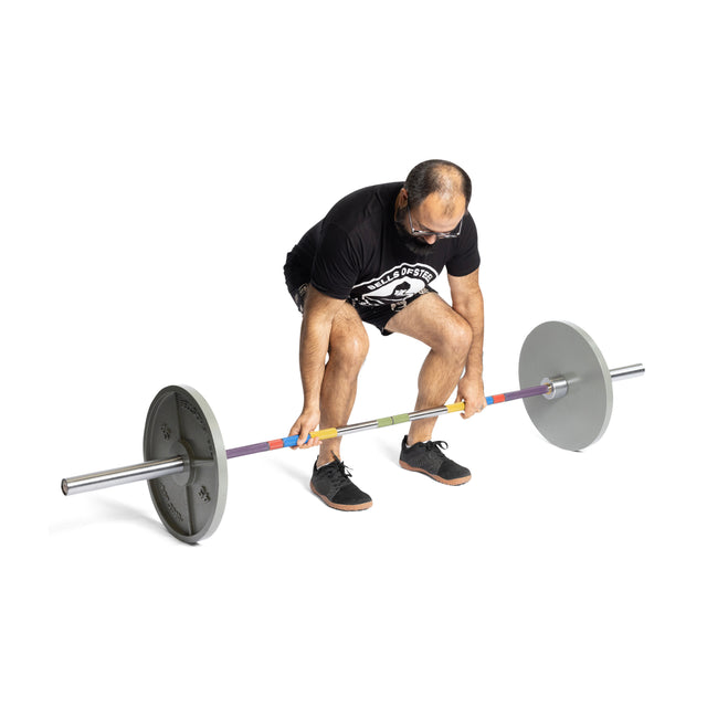 A person in a black t-shirt and shorts stands in a squat position, ready to powerlift with the Bells of Steel Hydra Seven Ring Bar and gray weight plates on a white background.