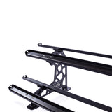 Close-up of a black metal roof rack with three parallel bars atop a vehicle, featuring geometric patterns in the mounting bracket, echoing those in Bells of Steel's Commercial Interchangeable Weight Rack - Components Only, set against a white background.