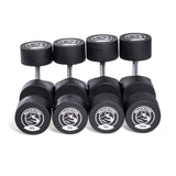 Five pairs of Bells of Steel Urethane Dumbbell Sets, labeled 85–100 lbs, are arranged in a row with circular logos on the ends—demonstrating commercial-grade quality for serious lifters.