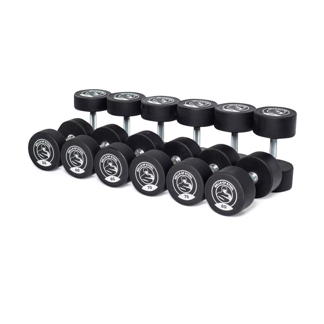 A set of commercial-grade Bells of Steel Urethane Dumbbells, featuring stainless steel heads, are neatly arranged in two rows. Weights range from 45 to 100 pounds, each with gleaming metallic handles and a logo on the side.