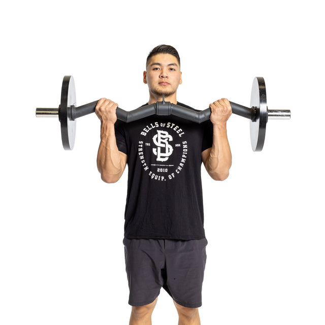 A person leans back slightly while lifting the Bells of Steel Fat Bar - Olympic Curl Bar Cable Attachment with both hands, enhancing their grip strength. They wear a black t-shirt with white text and black shorts against a plain white background.