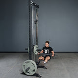 A man sits on the gym floor using the Bells of Steel Fat Bar - Olympic Curl Bar Cable Attachment for seated rows. Wearing a black T-shirt and gym shoes, he pulls the handlebar to his torso to build grip strength.