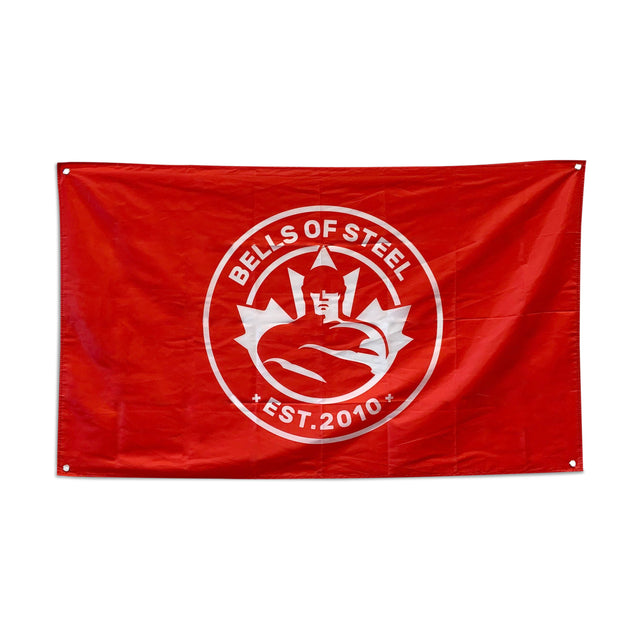 A red Bells of Steel gym flag displays a circular emblem of a stylized muscular figure encircled by gears. "BELLS OF STEEL" appears above, and "EST. 2010" below, in white—ideal for enhancing your home gym decor.