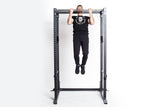 A man in black athletic wear performs a pull-up on the Bells of Steel Residential Power Rack (2.3" x 2.3", ⅝" holes), featuring metal j-cups, against a plain white background, highlighting home gym strength and versatility.