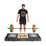 A man stands on the Bells of Steel Weightlifting Platform, eyes closed and arms down, preparing for a deadlift. He faces forward in a black shirt, shorts, and cap with white sneakers, ready before the Olympic barbell with red and green weights on sturdy deadlift pads.