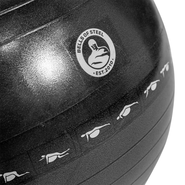 Close-up of a black Bells of Steel exercise ball featuring workout illustrations such as push-up positions and the "EST. 2010" text under the logo, perfect for boosting your routine.