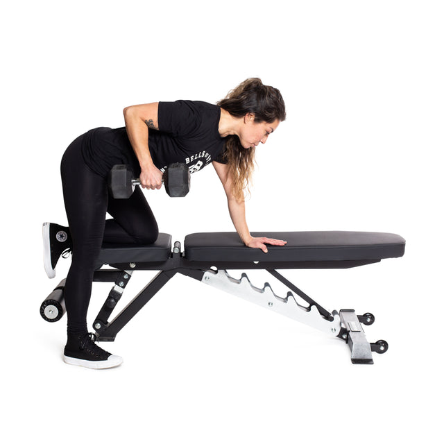 A person performs a single-arm dumbbell row on the Bells of Steel Flat / Incline / Decline Weight Bench - Commercial, which features a sturdy metal frame. They are dressed in a black shirt, black leggings, and black sneakers with white soles that perfectly complement the sleek design of the versatile bench.