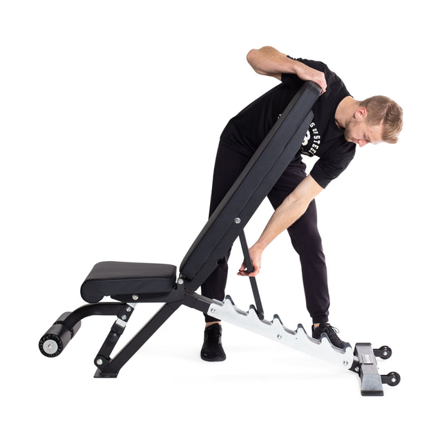 In a well-lit space, an individual in black t-shirt and pants adjusts the backrest of the **Bells of Steel Flat / Incline / Decline Weight Bench - Commercial**. This black and white bench, renowned for its heavy-duty steel frame, provides multiple incline options to enhance any fitness routine.