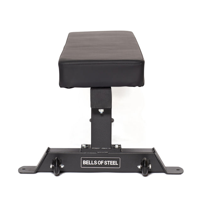 A black Powerlifting Flat Bench by Bells of Steel, viewed from the front, features a padded seat and brand name on the base. It's a light commercial grade bench with sturdy design, wheels for easy mobility, and supports up to 1,000lb capacity.