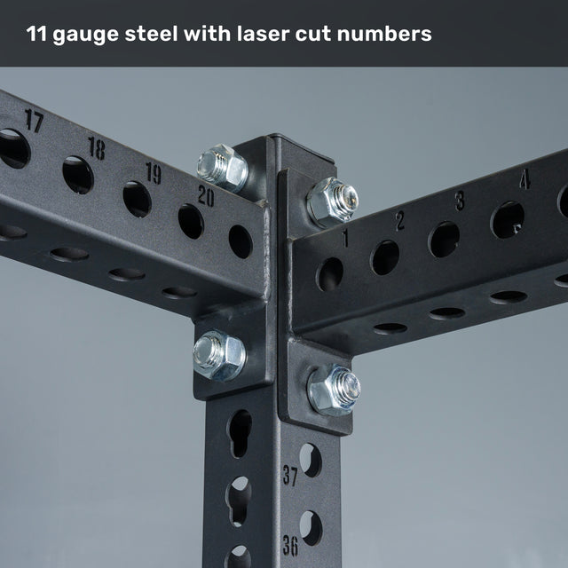Close-up of black steel beams from the Bells of Steel Manticore Flat Foot Power Rack Builder joined with bolts, featuring laser-cut numbers on the metal—ideal for any home gym setup. Text above reads: “11 gauge steel with laser cut numbers,” emphasizing the durable construction of this 3" x 3", 1" hole power rack.