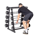 A person in a black shirt, shorts, and cap lifts a barbell from the Bells of Steel Fixed Barbell Rack, which holds multiple fixed-weight barbells of various sizes, set against a plain white background.