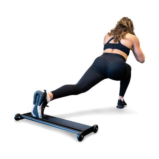 Wearing athletic gear, an individual performs a lateral lunge on a Bells of Steel Glute Ham Slider, praised for its space-saving design. They extend one leg sideways and bend the other while maintaining a squat against a plain white backdrop.