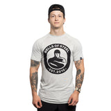 A young man in a backward black cap and a light grey Bells of Steel Bamboo T-Shirt stands against a white background, displaying tattoos on both arms and a neutral expression.