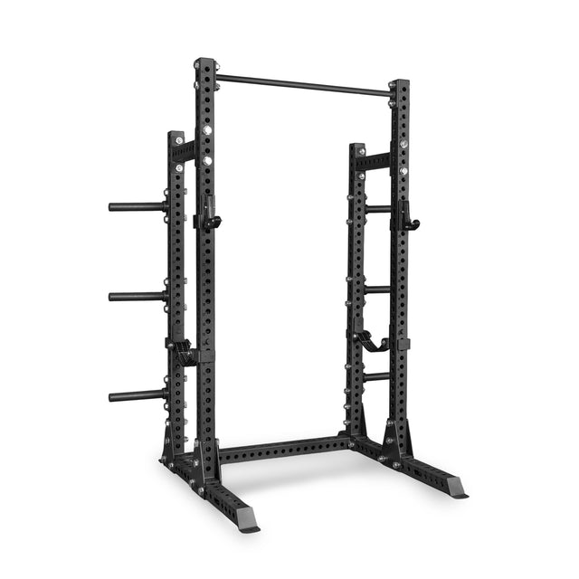 Introducing the Bells of Steel Manticore Half Rack - Prebuilt: a sleek black, heavy-duty metal rack featuring 3" x 3" uprights with 1" holes for versatile attachments, adjustable safety bars, an integrated pull-up bar on top, and plate holders on the sides—an ideal choice for weightlifting and strength training in your home gym.