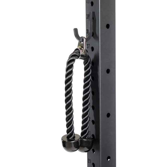 A black tricep rope with rubber ends hangs from a Bells of Steel Utility Hook on a metal gym rack with numbered holes, demonstrating organized storage for cable attachments.