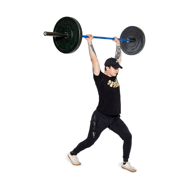 A person in athletic wear and a cap uses the Bells of Steel Multi-Purpose Olympic Barbell – The Utility Bar to perform an overhead lift, extending one leg forward in a lunge position, showcasing tattoos on their arms against a plain white background.