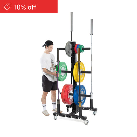 A person stands by the Bells of Steel Hydra Bumper Plate Tree Builder, a modular rack for home gym plate storage, with colorful weight plates and a barbell. A "10% off" banner appears in the top left corner.