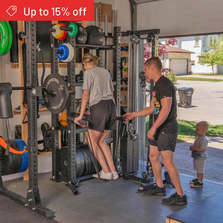 A woman does triceps dips at home, supported by a man, while a child stands nearby. Bells of Steel Hydra Storage Builder and other fitness equipment are visible, with a red "Up to 15% off" banner in the top left corner.