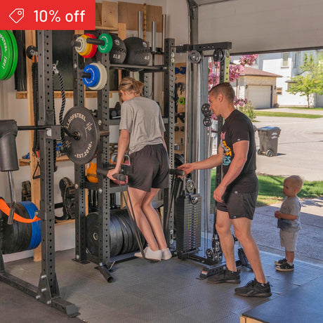 A woman does tricep dips on parallel bars in a garage gym while a man supervises and a child watches. Weightlifting gear is neatly organized on the Bells of Steel Hydra Storage Builder. A "10% off" banner appears in the top left corner.