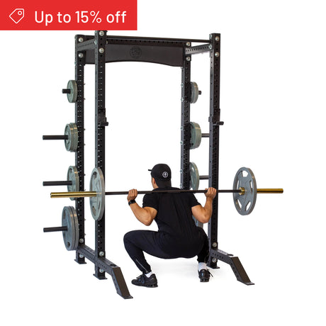 A person in black workout clothes squats with a barbell inside the Bells of Steel Hydra Collegiate Power Rack Builder (3" x 3", ⅝" Holes), loaded with weights. A red banner in the corner says "Up to 15% off." Ideal for any home gym.