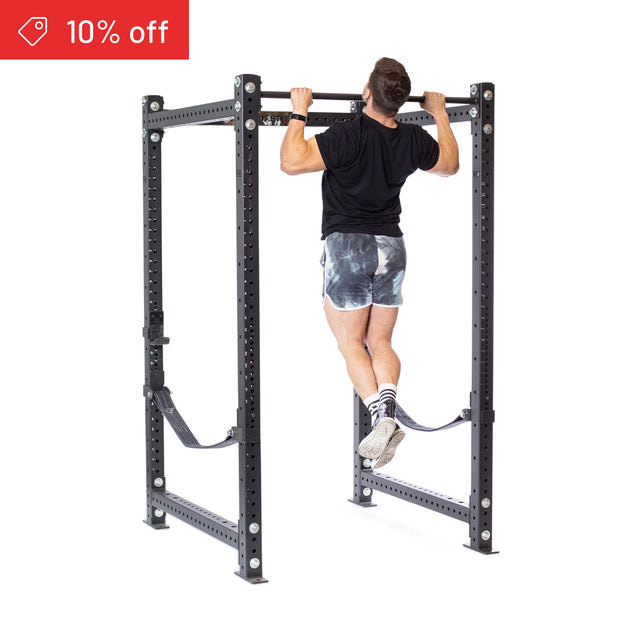 A man in a black shirt and patterned shorts performs a pull-up on the Bells of Steel Hydra Four Post Power Rack Builder (3" x 3", ⅝" holes). A red "10% off" banner appears in the top left on a white background. Perfect addition to any home gym.