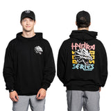 A man wears a buttery soft bamboo blend Bamboo Hoodie from Bells of Steel, matched with a cap. The front displays a small logo on the chest, and the back features a large "Hydra BASS Series" graphic with colorful elements. He pairs it comfortably with gray shorts.