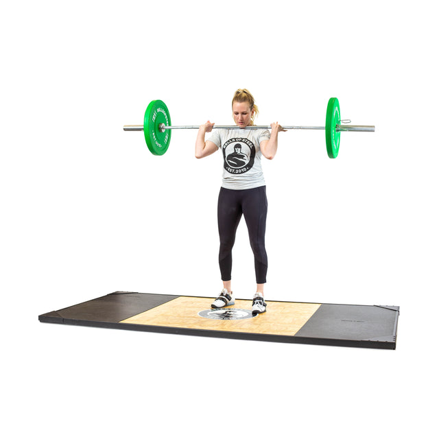 A woman in a light t-shirt, black leggings, and athletic shoes stands on a platform with a barbell loaded with Bells of Steel Colored Bumper Plate Sets across her shoulders, getting ready to lift.
