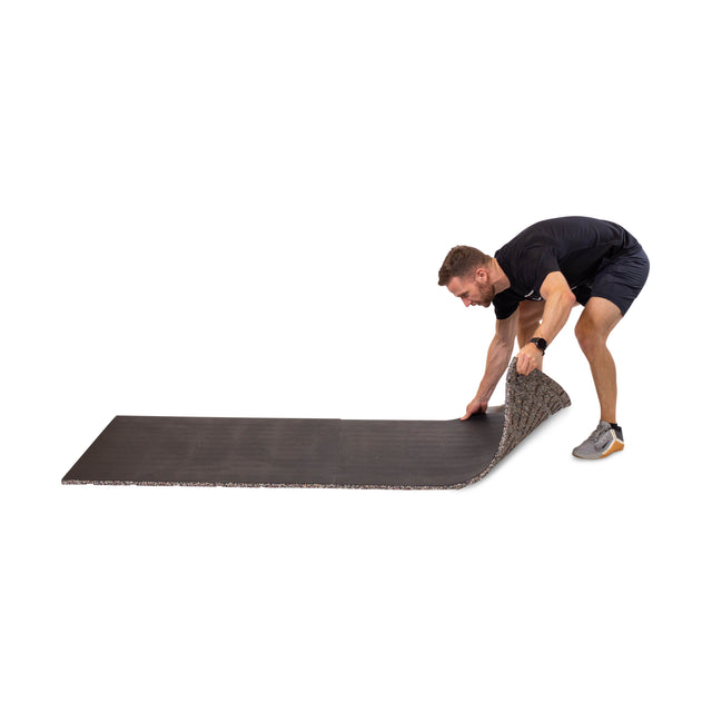 A person in athletic attire unrolls a Bells of Steel Rubber Flooring Gym Mat, 39" x 39", made from recycled rubber, against a white background. They bend over, using one hand to lift while the other steadies the mat.