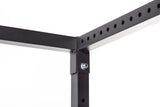 Close-up of a Bells of Steel Residential Power Rack (2.3" x 2.3", ⅝" holes) corner, showing black metal bars joined with a bolt and nut; one bar displays evenly spaced holes along its length against a white background.