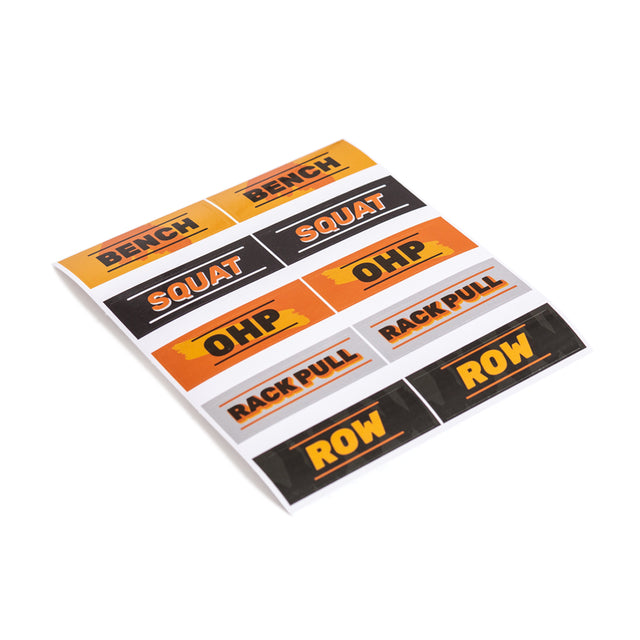 Bells of Steel Stickers: A sheet of rectangular exercise labels with "BENCH," "SQUAT," "OHP," "RACK PULL," and "ROW" in bold. Crafted with quality adhesive, they come in orange, yellow, and black, arranged in three rows.