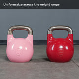 Two Bells of Steel Competition Kettlebells, one pink (8kg) and one red (32kg), sit on a gym floor. Both are identical in size, demonstrating the uniform size across the weight range.