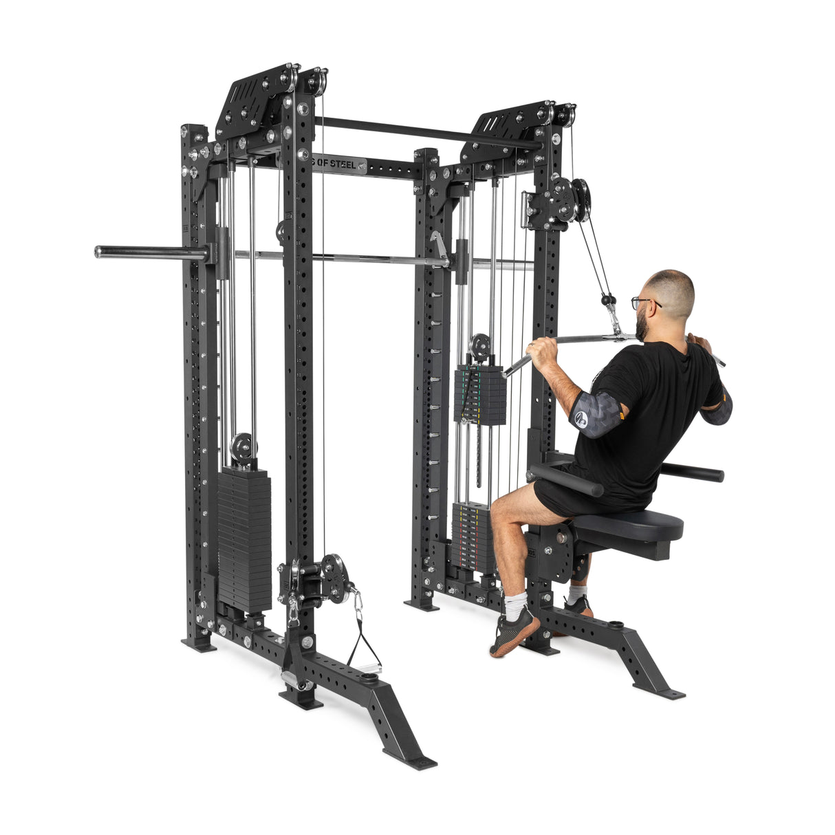 A person exercises on the durable THE KOLOSSOS - Smith Functional Trainer by Bells of Steel, smoothly pulling down a bar connected to the weight stack. The sturdy black machine stands alongside a power rack, all with multiple handles and visible weights awaiting action.