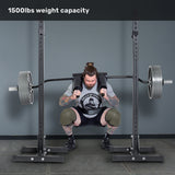 A tattooed man performs barbell squats on leg day using the Bells of Steel Safety Squat Bar - The SS4 in a gym rack, lifting a heavily loaded bar with "1500lbs weight capacity" displayed above.