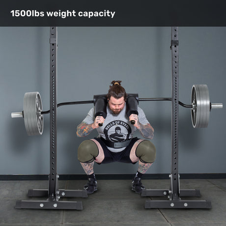 A tattooed man performs barbell squats on leg day using the Bells of Steel Safety Squat Bar - The SS4 in a gym rack, lifting a heavily loaded bar with "1500lbs weight capacity" displayed above.