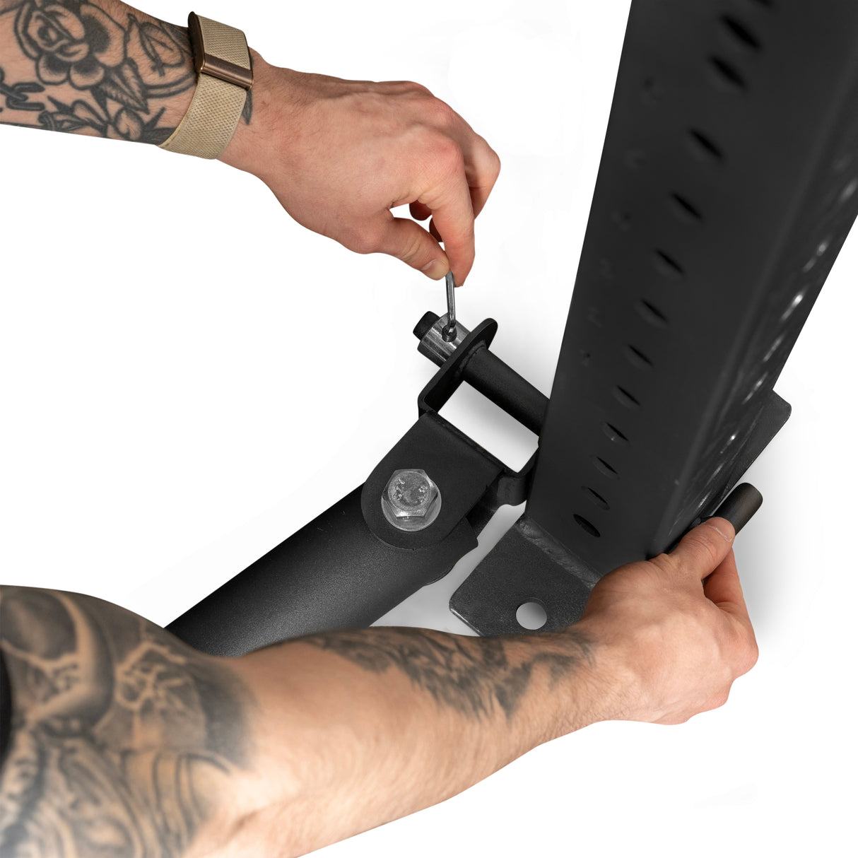 Two tattooed arms assemble a Bells of Steel Landmine Rack Attachment by attaching a metal bracket with a tool, utilizing the structure's adjustable holes for an explosive workout. The person wears a watch on one wrist.