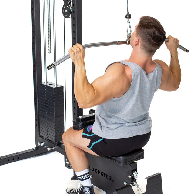 A man in a gray tank top and black shorts uses the Bells of Steel Lat Pulldown Low Row Machine for his lat pulldown exercise.