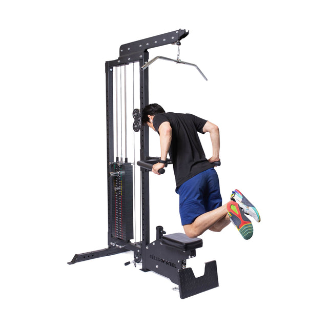 A person uses the Bells of Steel Lat Pulldown Low Row Machine for a tricep dip. They are wearing a black shirt and blue shorts. The multi-functional machine's weight stack is visible against a plain white background.