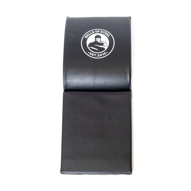 The Luxury Sit Up Mat by Bells of Steel is black, has a convenient fold in the middle, and features a logo with "Bells of Steel," a bell illustration, and "Est. 2010" text at the top. Ideal for core workouts, it supports lumbar curvature to enhance your exercises.