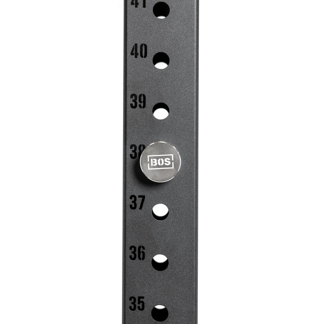 Close-up of a black metal power rack with numbers 35 to 41. A Bells of Steel "BOS" magnetic rack attachment pin is inserted at position 38, and the rack has evenly spaced holes for each number.