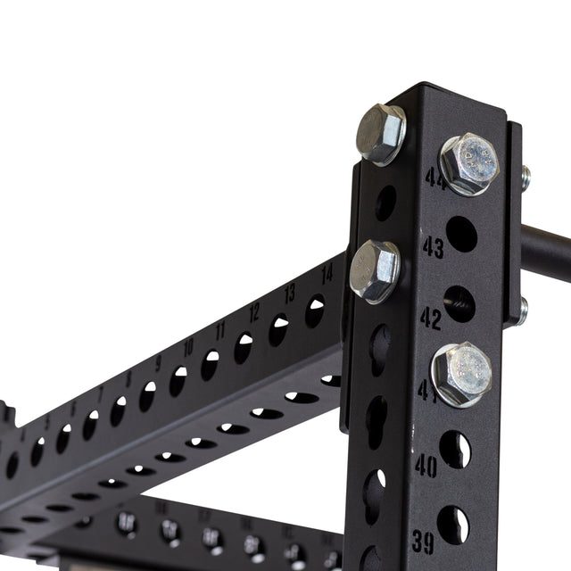 Close-up of the Bells of Steel Manticore Four Post Power Rack Builder, featuring 3" x 3" black metal with 1" numbered holes for adjustments. Large silver bolts secure the sturdy horizontal and vertical bars, highlighting its robust construction and modular design for a home gym.