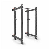 The Manticore Folding Power Rack - Prebuilt by Bells of Steel features black 3"x3" uprights, 1" holes, and red safety pins for weightlifting and strength training in a home gym, shown against a white background.