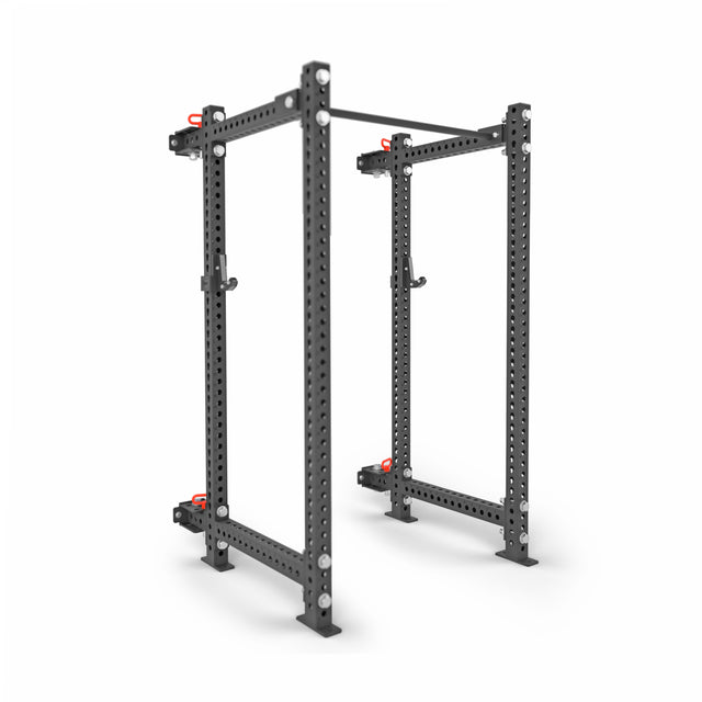The Manticore Folding Power Rack - Prebuilt by Bells of Steel features black 3"x3" uprights, 1" holes, and red safety pins for weightlifting and strength training in a home gym, shown against a white background.