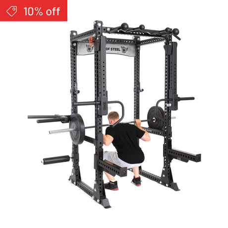 A man squats with a barbell in the Bells of Steel Manticore Flat Foot Power Rack Builder (3" x 3", 1" Holes). A red "10% off" sale tag appears in the top left—ideal for enhancing your home gym.