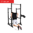 A person in a black shirt and gray shorts does dips on the Bells of Steel Manticore Half Rack Builder (3" x 3", 1" Holes), ideal for home gyms. A red "10% off" banner appears in the top left corner. The background is white.