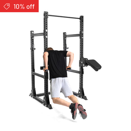 A person in black and gray performs tricep dips on the Bells of Steel Manticore Half Rack Builder (3" x 3", 1" holes). A red "10% off" banner appears at the top left, set against a white background to highlight your home gym.